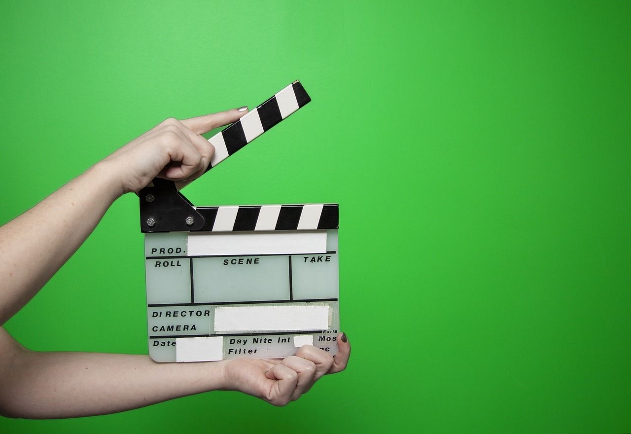 Hand hält offene Filmklappe auf grünem HIntergrund