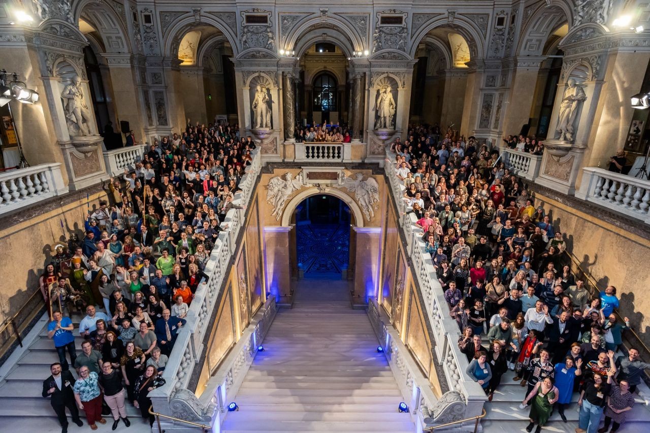 Gruppenfoto: Konferenzteilnehmer*innen stehen auf der großen Eingangstreppe im Naturhistorischen Museum Wien und jubeln in die Kamera